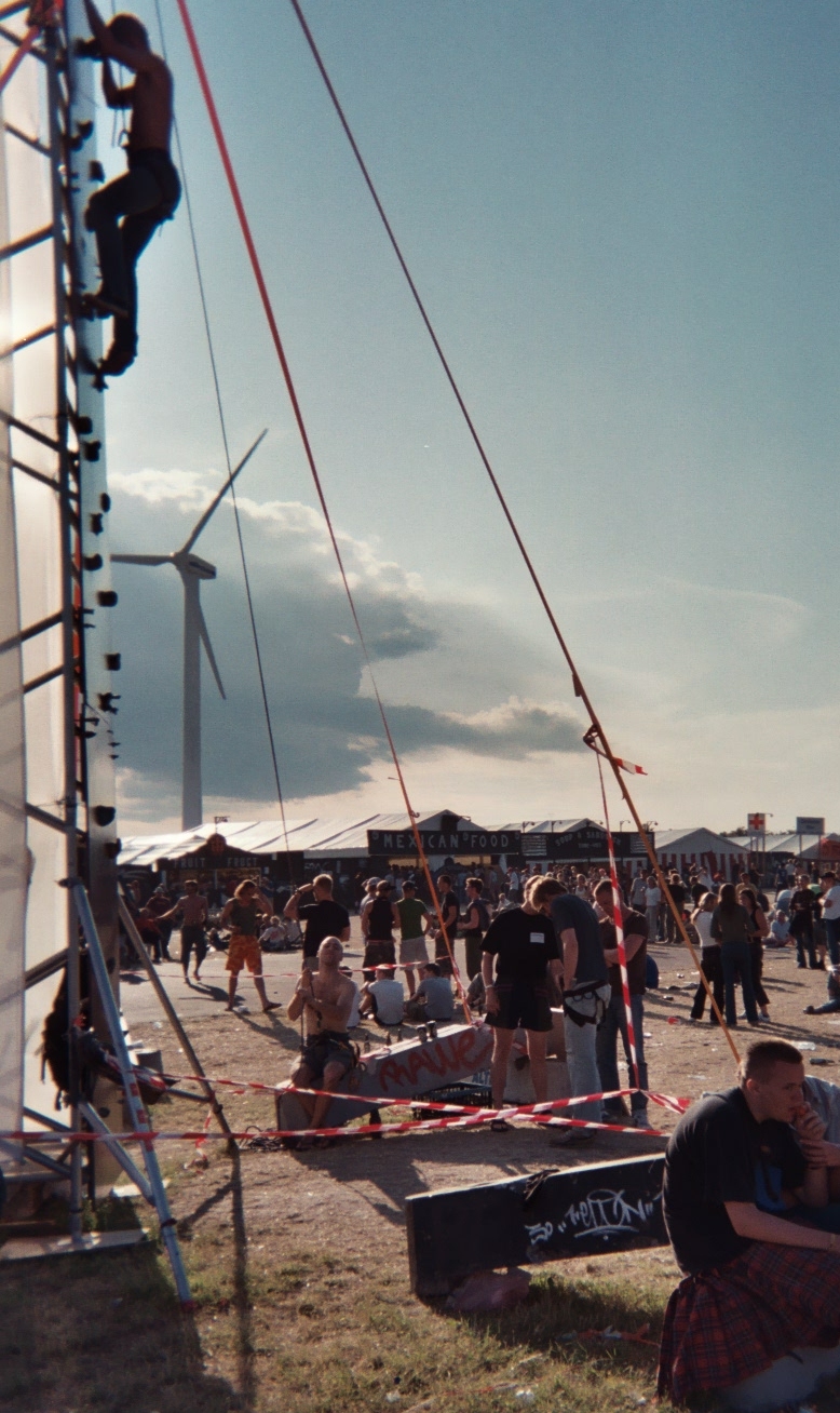 Farbphoto: Ein Mensch klettert, gesichert von Mitgliedern des "Roskilde climbing Clubs", eine künstliche Wand hinauf. Auf dem ROSKILDE FESTIVAL in Roskilde in Dänemark.  Im Juni 2003. Photo: Erwin Thomasius.